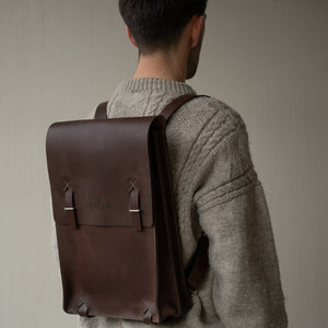 Man wearing a brown leather backpack against a plain background